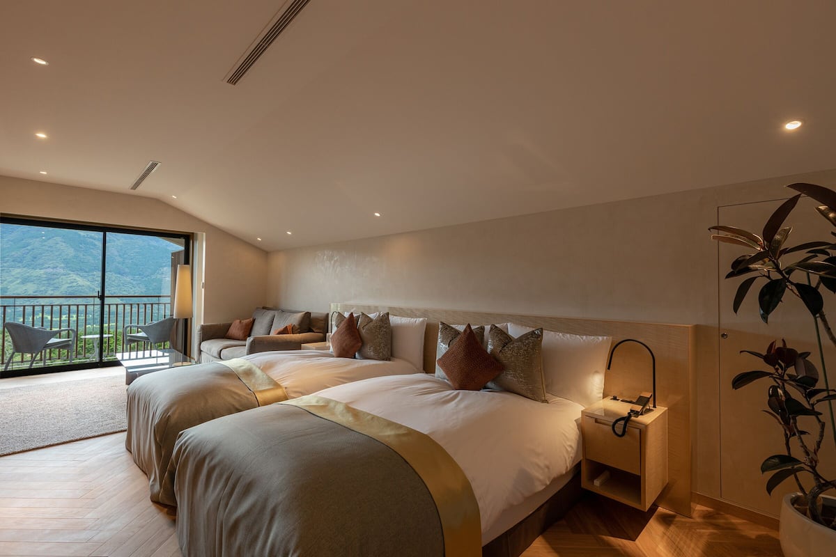 Ein modernes Hotelzimmer mit einem großen Bett, einem Nachttisch, einem kleinen Tisch daneben und einem Balkon mit Blick auf die Berge.