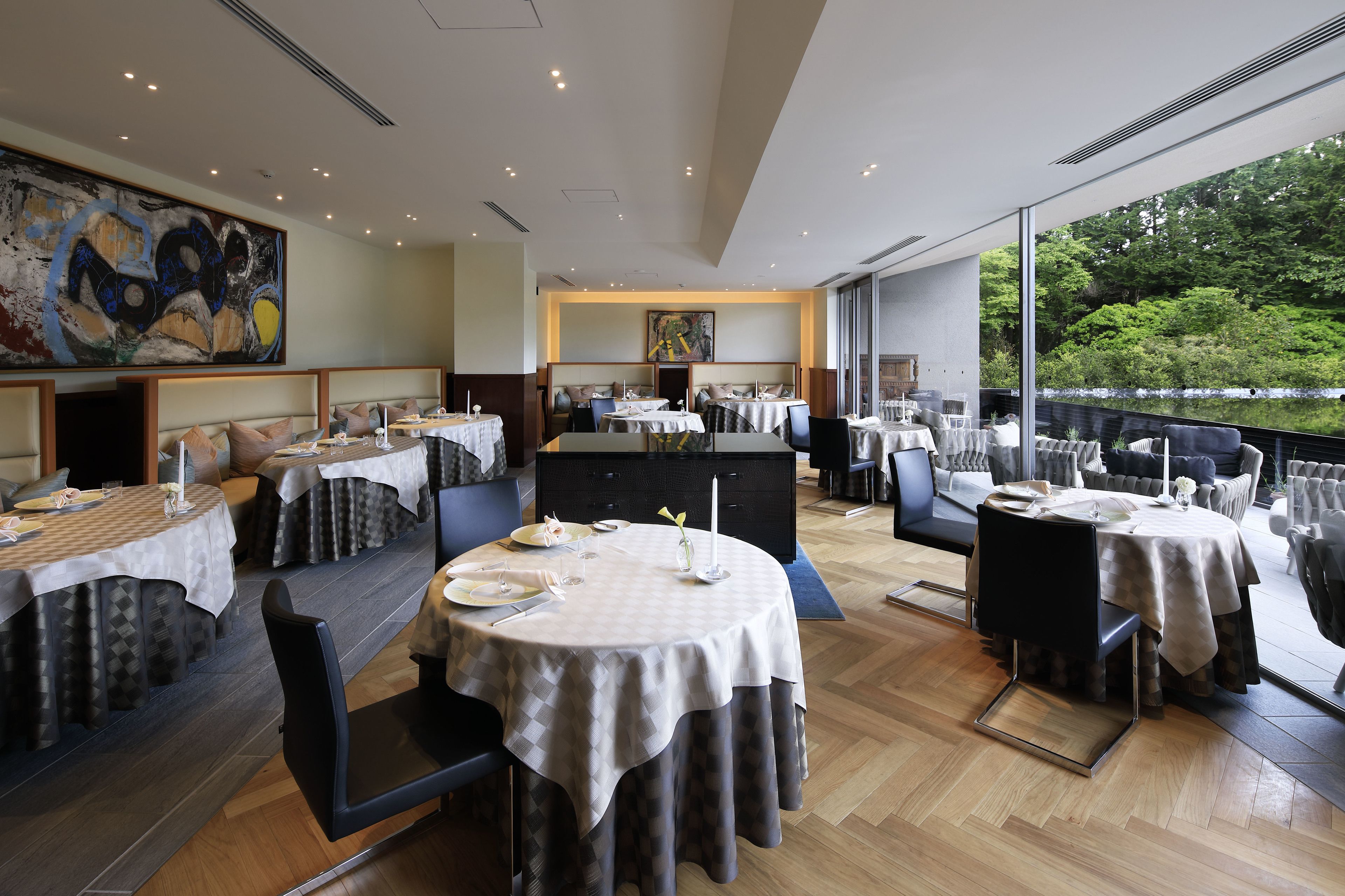 A restaurant with round tables, high ceilings, and large windows overlooking a green landscape.