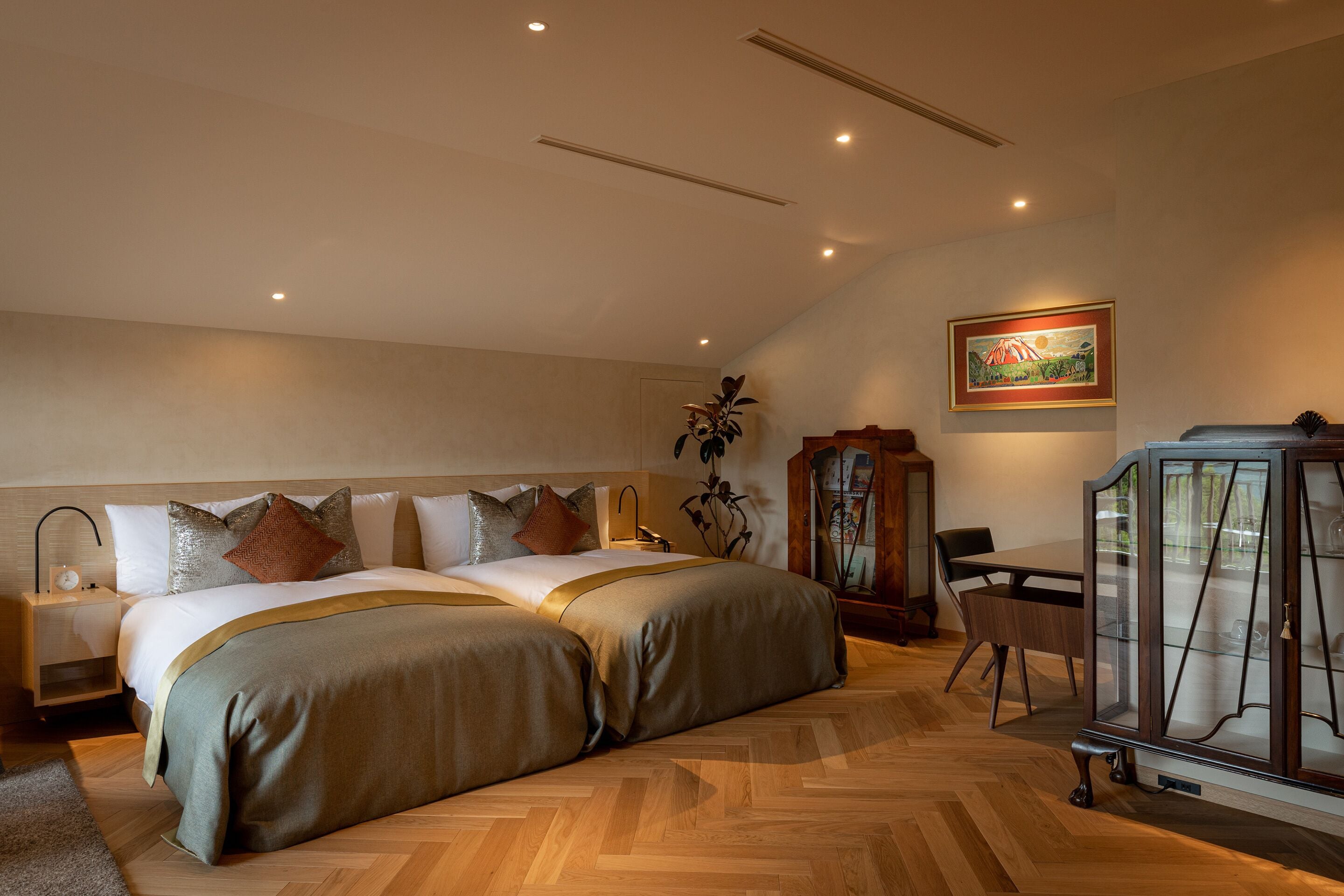 Un dormitorio con dos camas, piso de madera, mesita de noche, una mesa y un armario.