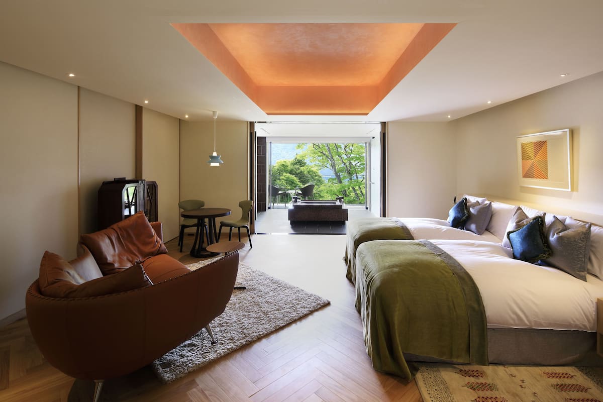 Ein modernes Hotelzimmer mit einem großen Bett, einer Sitzecke, einem Fernseher und einem Balkon mit Blick auf Bäume.
