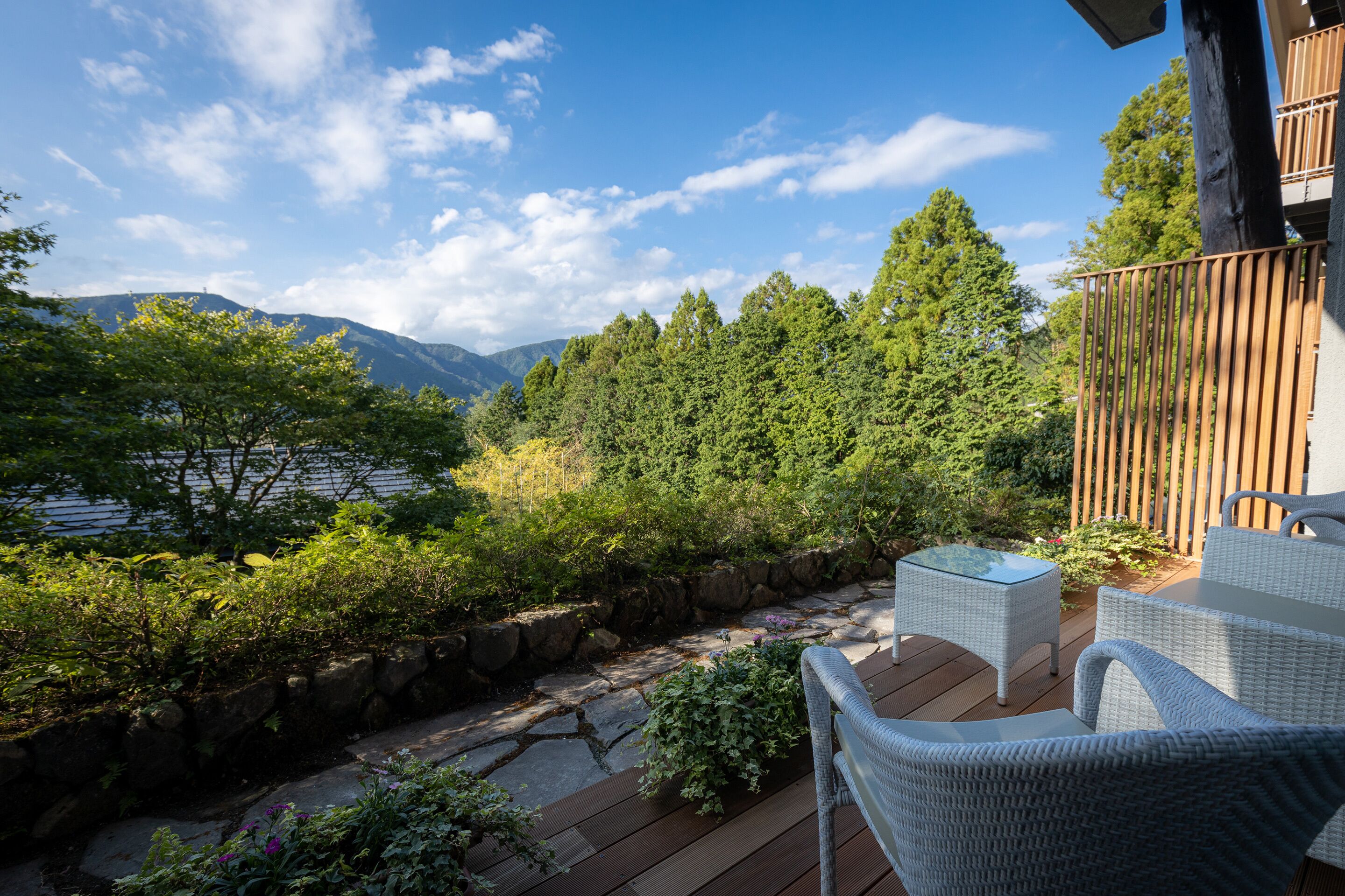 Terraza con mobiliario de mimbre con vistas a un jardín y montañas.