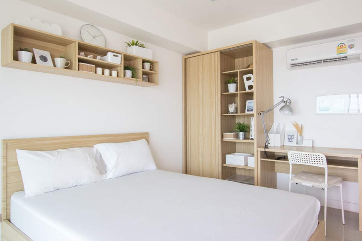 A bedroom with a bed, a desk, and shelves with various items.