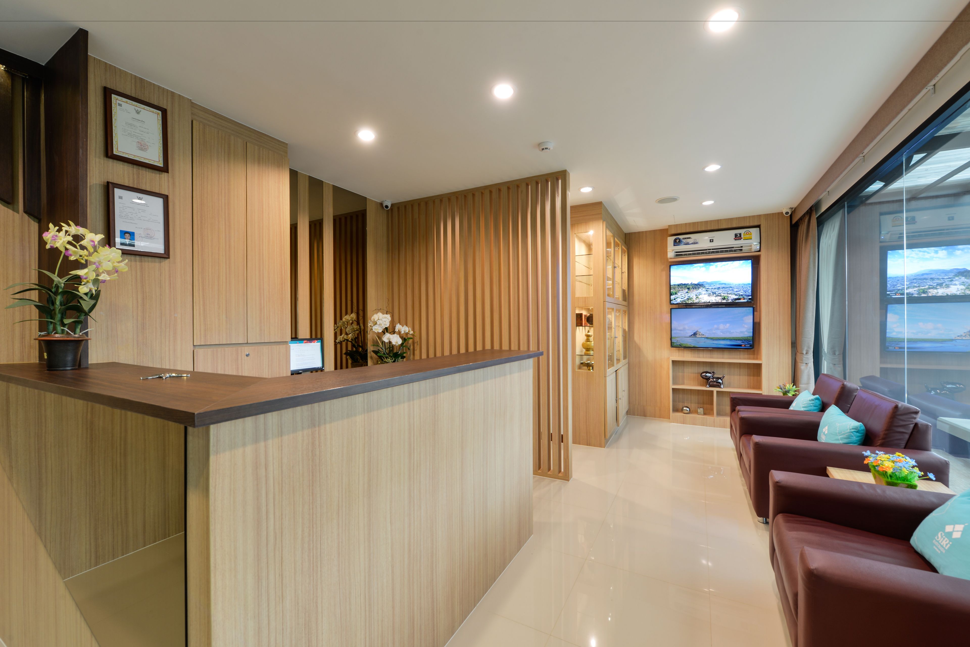 A reception area with a wooden reception desk, framed certificates, a flat-screen TV, and a seating area with leather sofas.