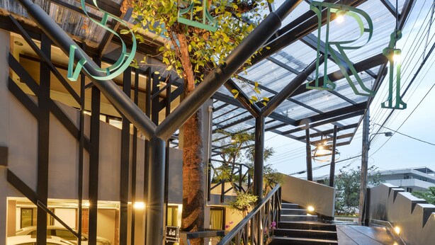 Een modern gebouw met een trap naar een parkeerterrein, omringd door groen en verlicht met sfeerverlichting.