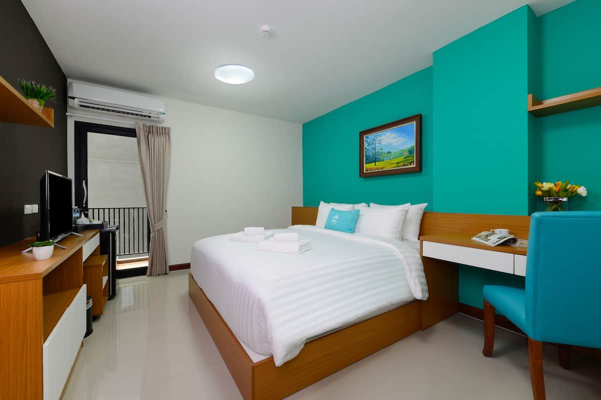 A modern hotel room with a bed, desk, chair, and a painting on the wall.