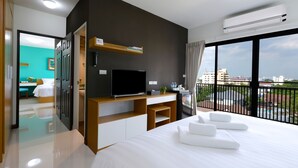 Een moderne hotelkamer met een groot bed, een flatscreen televisie, een bureau met een computer en een balkon met uitzicht op de stad.