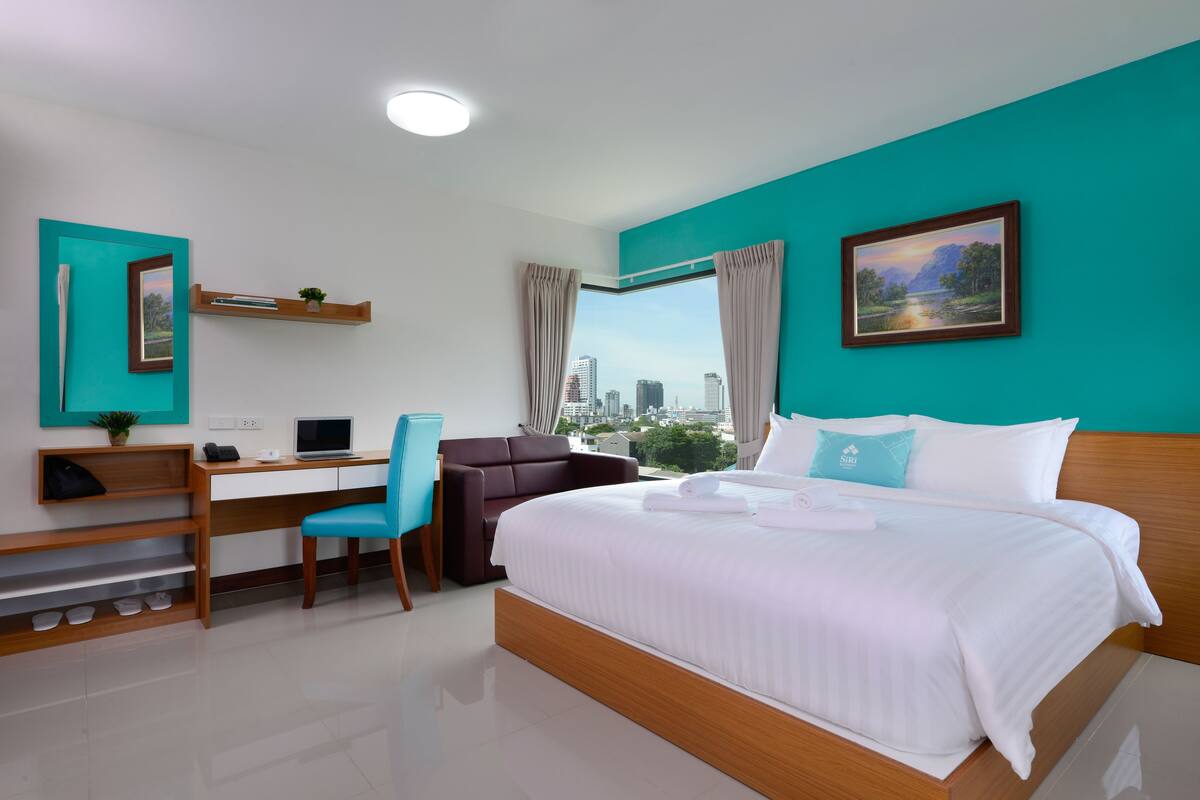 A modern hotel room with a bed, desk, chair, and a city view.
