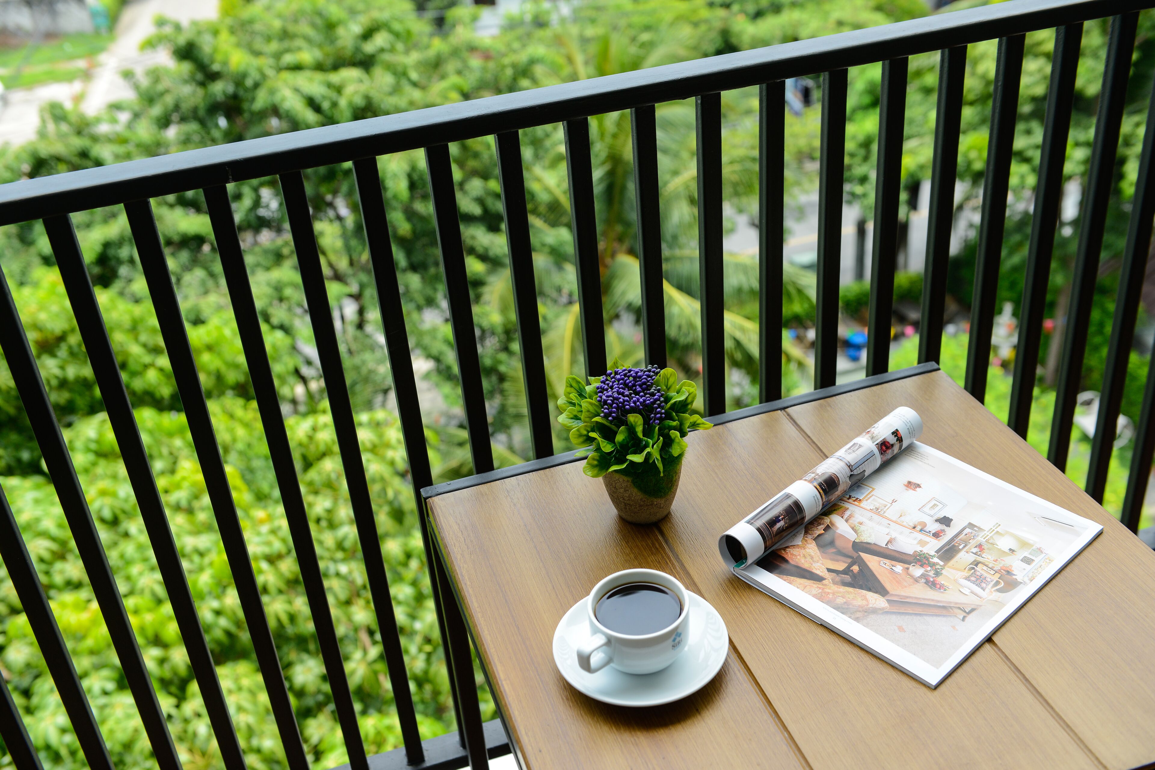 A wooden table with a cup of coffee, a small potted plant, and a magazine on a balcony.