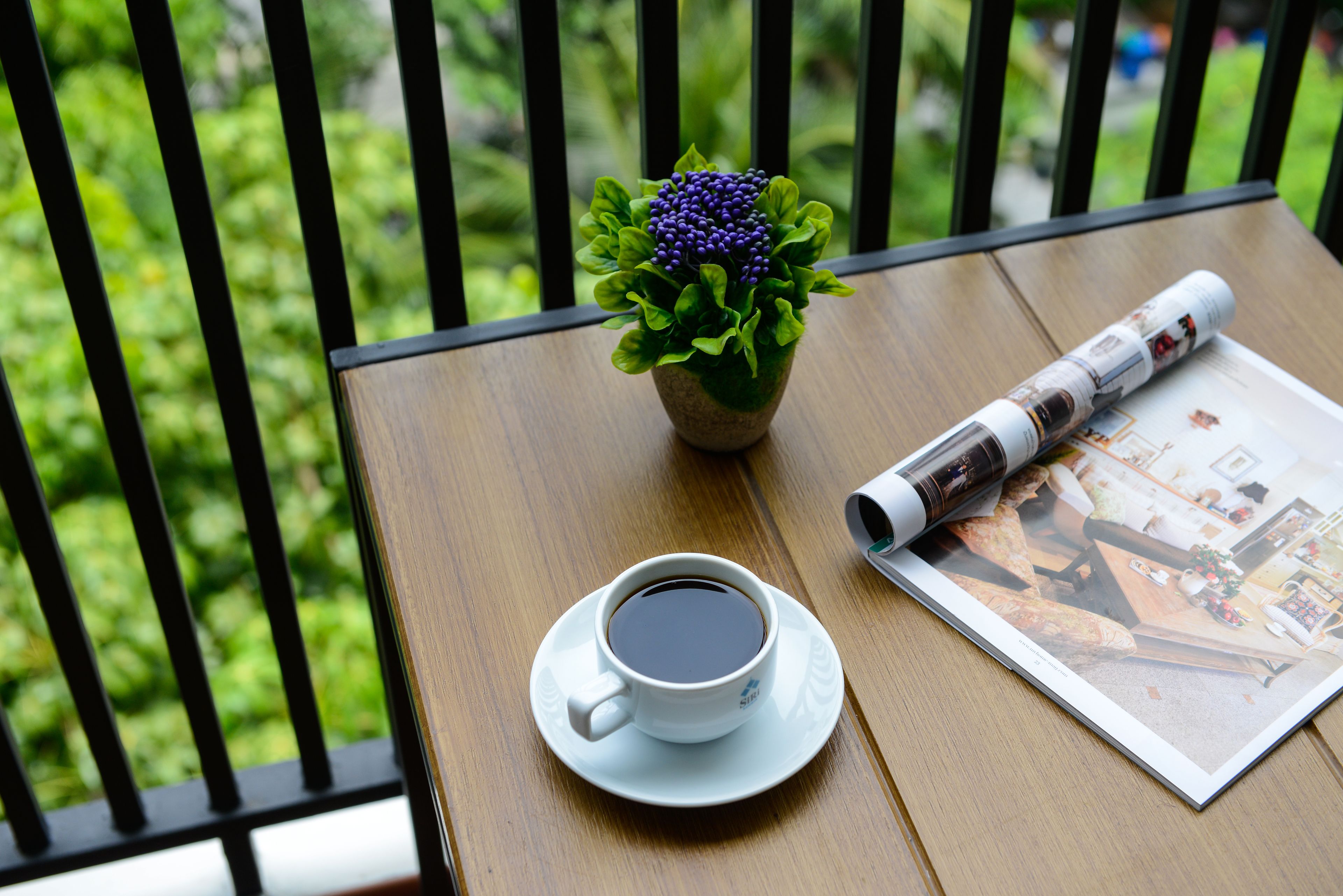 A cup of coffee on a table with a magazine and a potted plant.