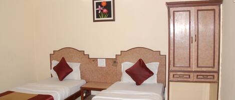 A hotel room with two beds, a wooden wardrobe, and a wall-mounted light fixture.