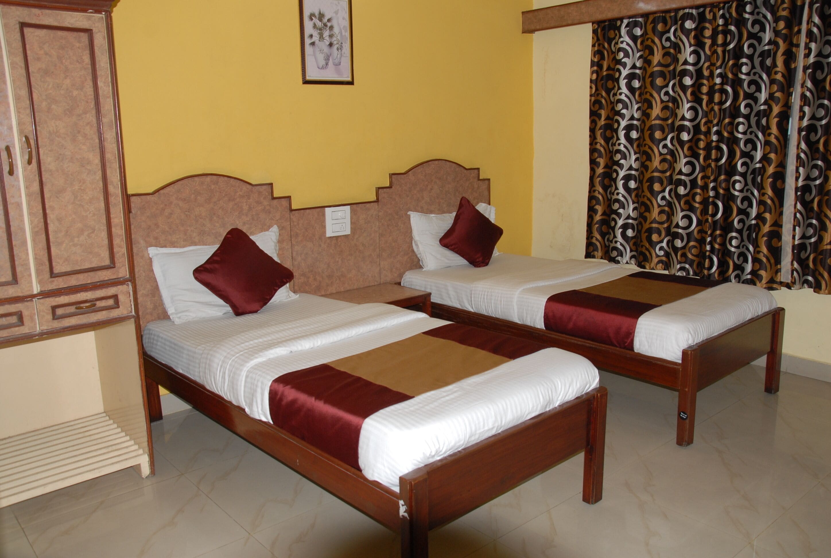 Two wooden beds with white and red bedding, a wooden wardrobe, and a patterned curtain.