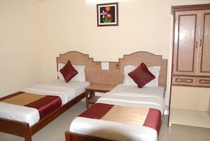 A room with two single beds, each with a wooden headboard, a small bedside table, and a red and beige bedspread. - Hotel Bhavani Lodge (Hyderabad)