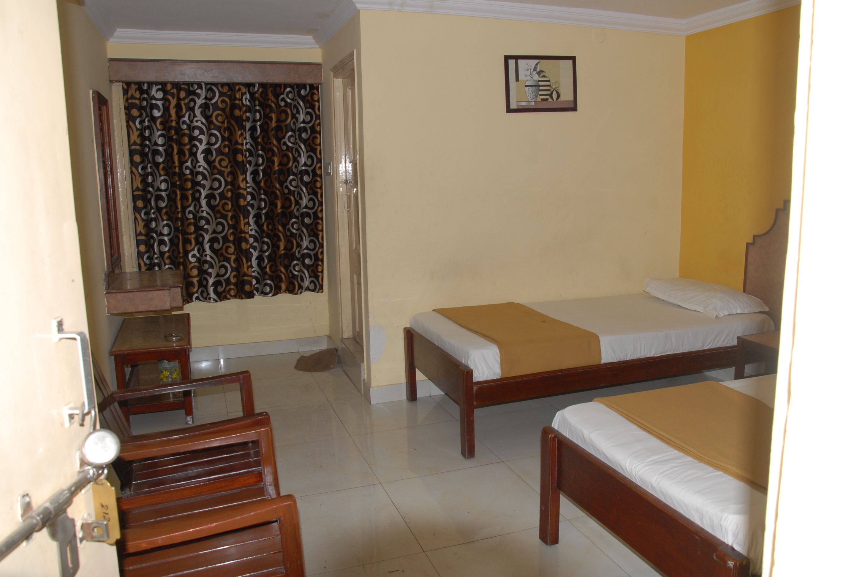 A hotel room with two single beds, a wooden desk, a chair, and a curtain with a swirling pattern.