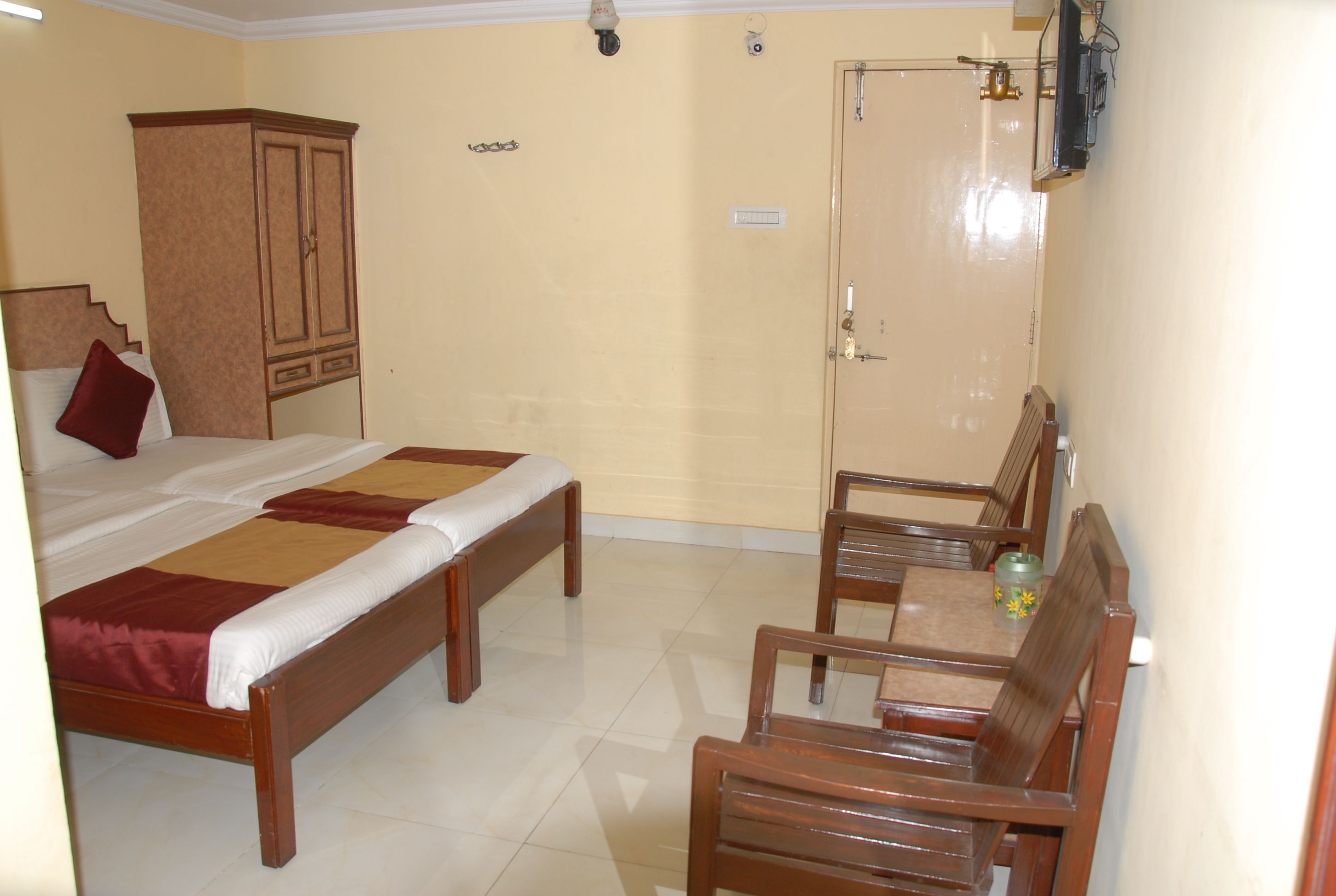 A hotel room with a bed, a wooden wardrobe, a table with chairs, and a door.