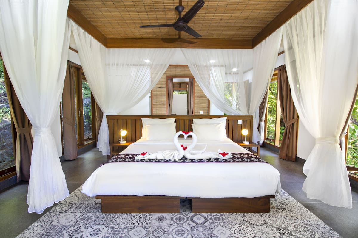 Una cama grande con estructura de madera, ropa de cama blanca y un diseño decorativo de cisne en la colcha.