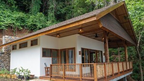 Una casa de madera de dos pisos con balcón, base de piedra y un jardín con plantas en macetas.