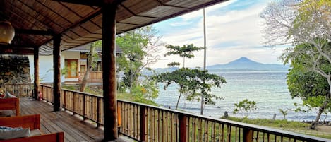 A wooden deck with a bamboo railing overlooking a body of water and a mountain in the distance.