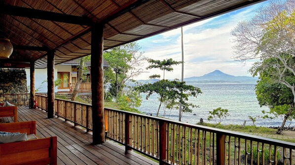 A wooden deck with a bamboo railing overlooking a body of water and a mountain in the distance.