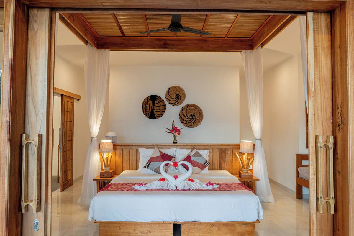 Habitación de hotel con techo de madera, cama con ropa blanca, dos mesitas de noche con lámparas y una pared decorada con tres tapices tejidos.