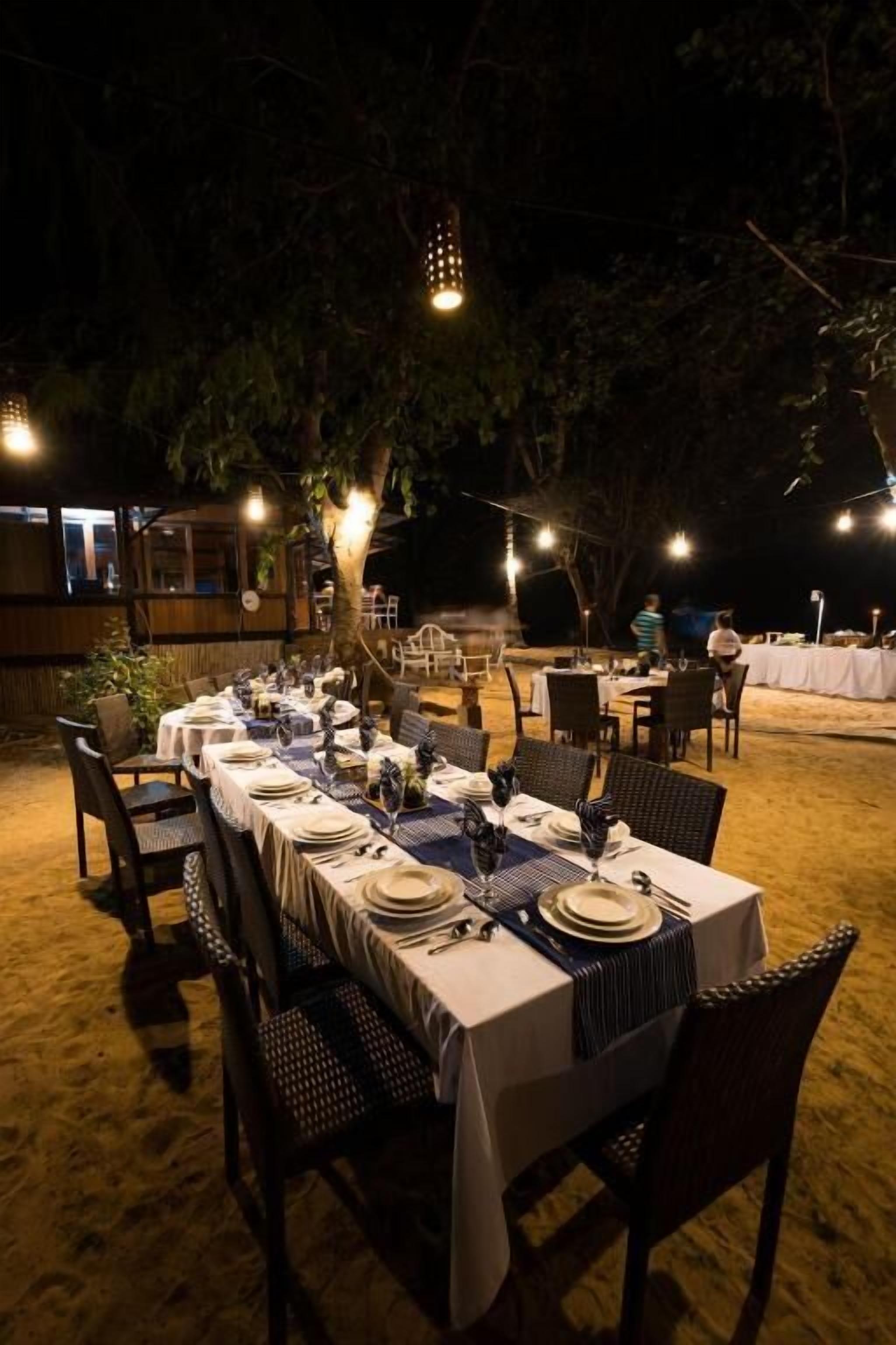 An outdoor dining area with tables set for multiple guests, surrounded by chairs and covered with tablecloths.