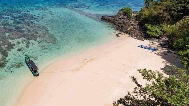 Una playa con aguas turquesas cristalinas, una orilla arenosa y un bote amarrado a la izquierda.
