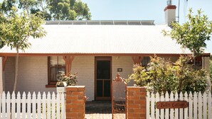 A house with a white picket fence, a brick entrance, and a sign that reads "Bell's Cottage." - Bell's Cottage Collective (West Bendigo)