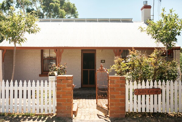 A house with a white picket fence, a brick entrance, and a sign that reads "Bell's Cottage." - Bell's Cottage Collective (West Bendigo)