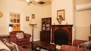 A traditional living room with a fireplace, a wooden coffee table, and two patterned armchairs. - Bell's Cottage Collective (West Bendigo)