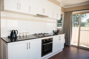 A modern kitchen with white cabinets, a black countertop, and stainless steel appliances. - Bell's Cottage Collective (West Bendigo)