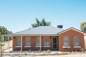 A single-story brick house with a gabled roof, a front porch, and a small garden area. - Bell's Cottage Collective (West Bendigo)