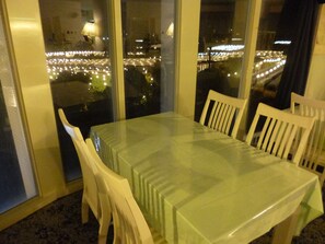 Ein Essbereich mit einem Glastisch und weißen Stühlen, große Fenster mit Blick auf eine nächtliche Skyline.