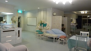 A hotel room with a sitting area featuring a sofa, a small table, and a decorative mirror. There is a separate dining area with a table and chairs. - Hotel Shalala (Okinawa)