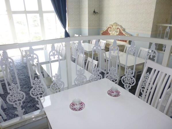 A dining area with white ornate chairs and tables, a blue carpet, and a view of the outside through large windows.