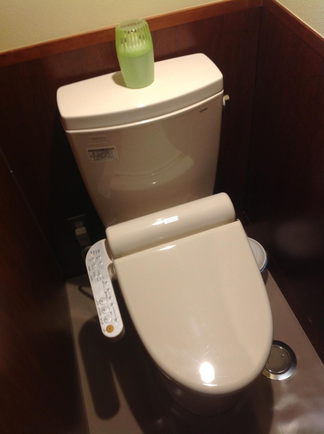 A toilet with a control panel and a green bidet head.