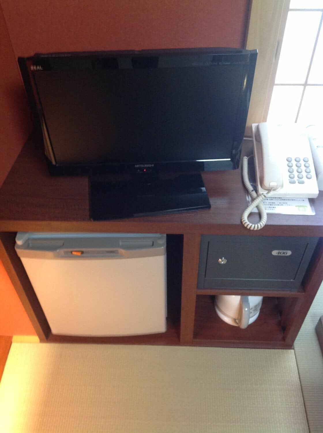 Une chambre d’hôtel équipée d’un téléviseur à écran plat, d’un téléphone, d’un mini-réfrigérateur et d’un petit placard.