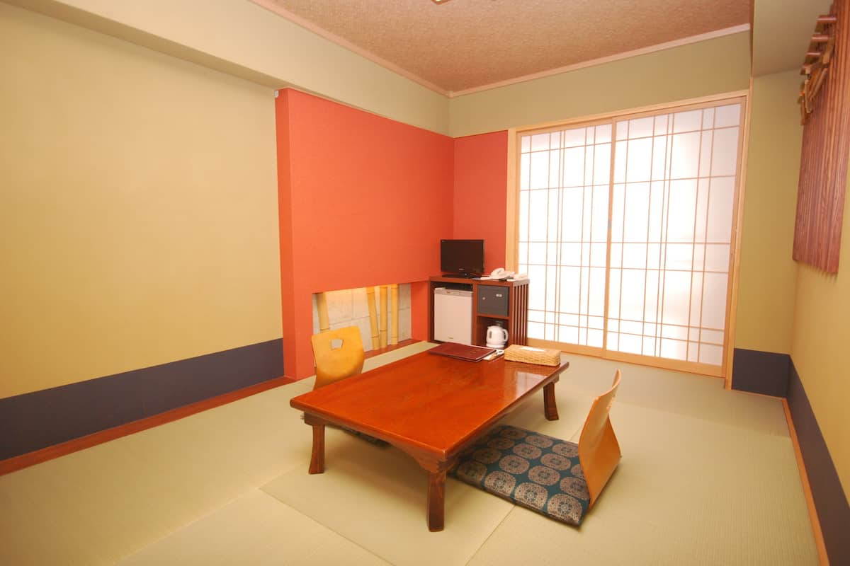 A traditional Japanese room with tatami flooring, a low wooden table, a sofa, a television, and a sliding shoji screen.