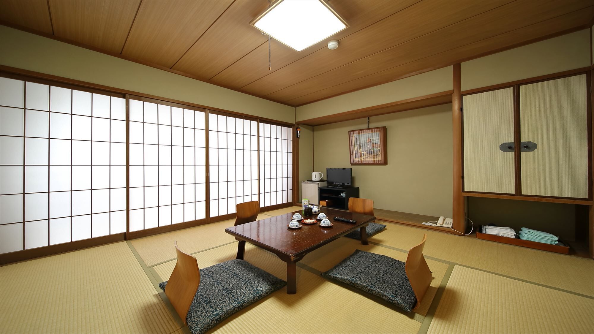A traditional Japanese room with tatami flooring, a low table with cushions, a television, and sliding doors.