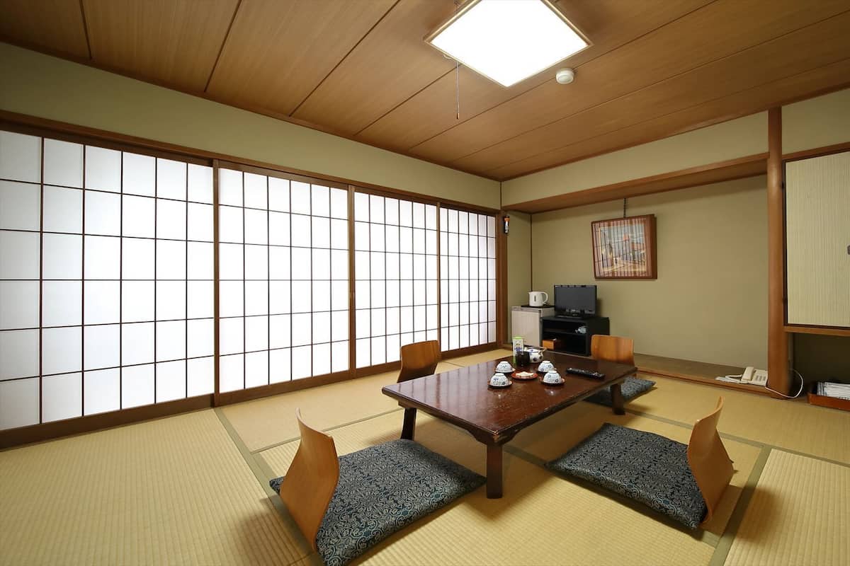 Una habitación japonesa tradicional con suelo de tatami, una mesa baja con cojines, un televisor y puertas correderas.