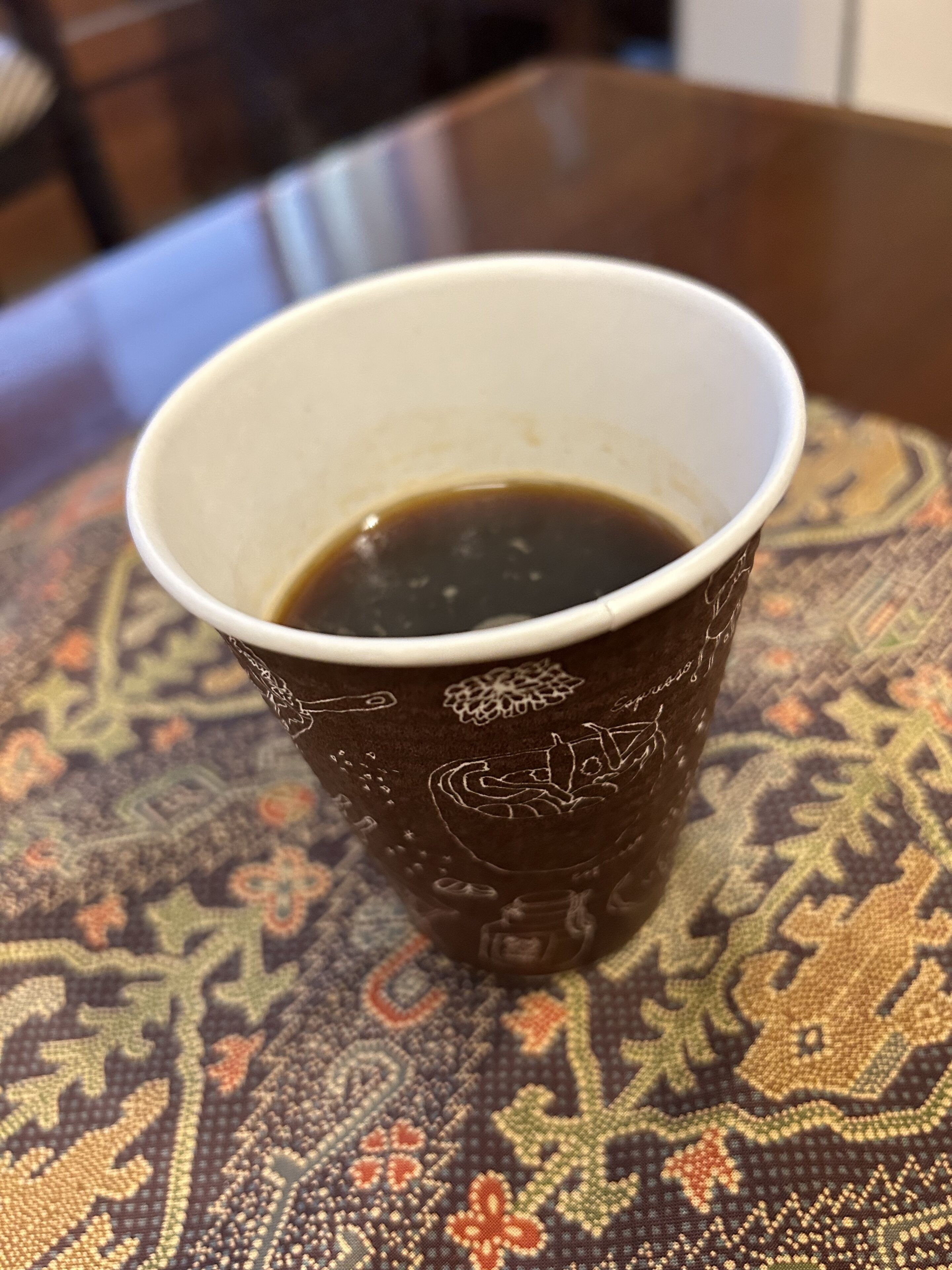A cup of coffee on a patterned tablecloth.