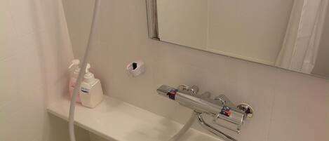 A bathroom with a bathtub, a handheld showerhead, a handheld massager, and a bottle of hand soap.