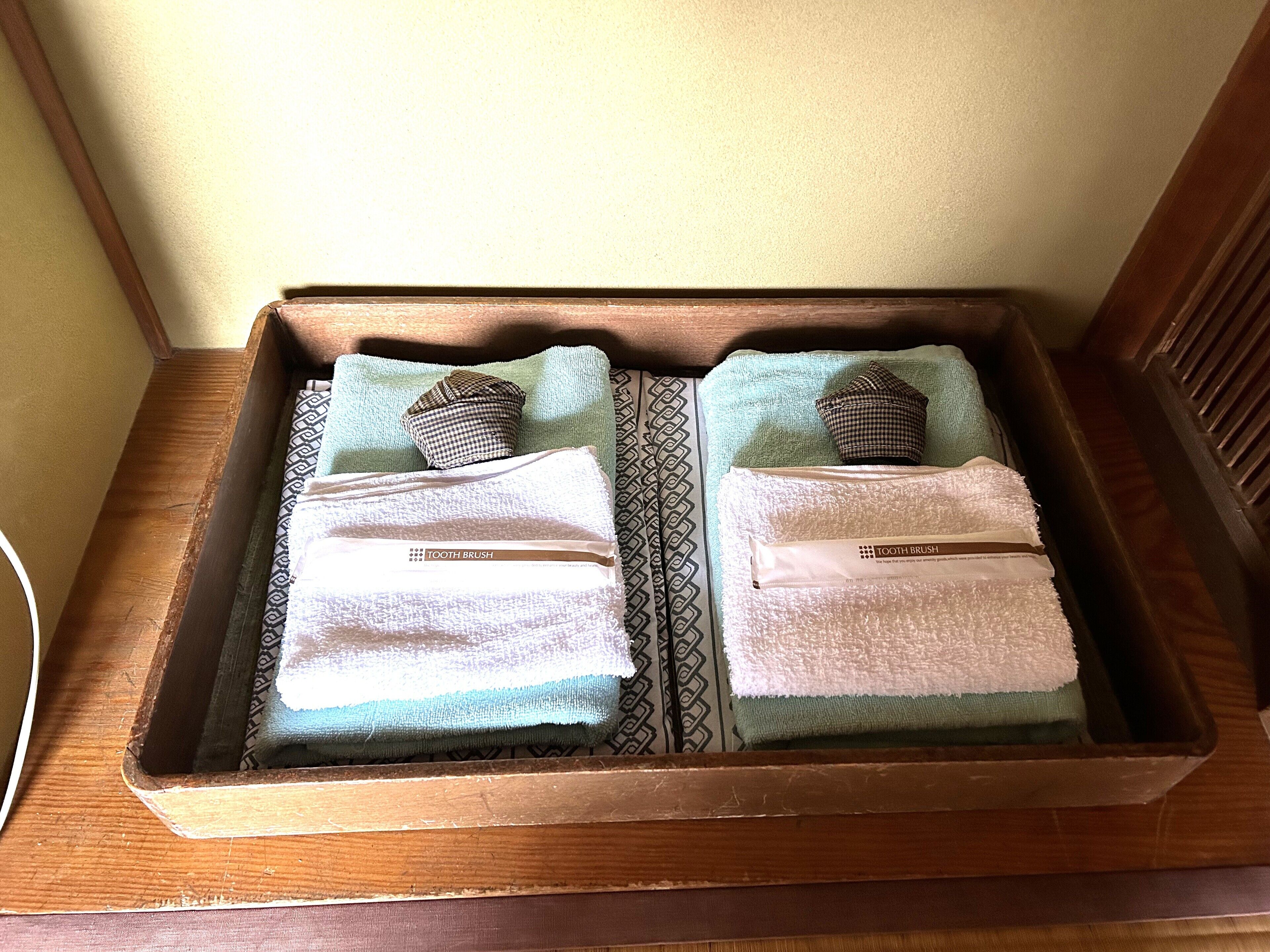 A wooden tray with two towels and two pillows, each with a 'TOOTH BRUSH' label.