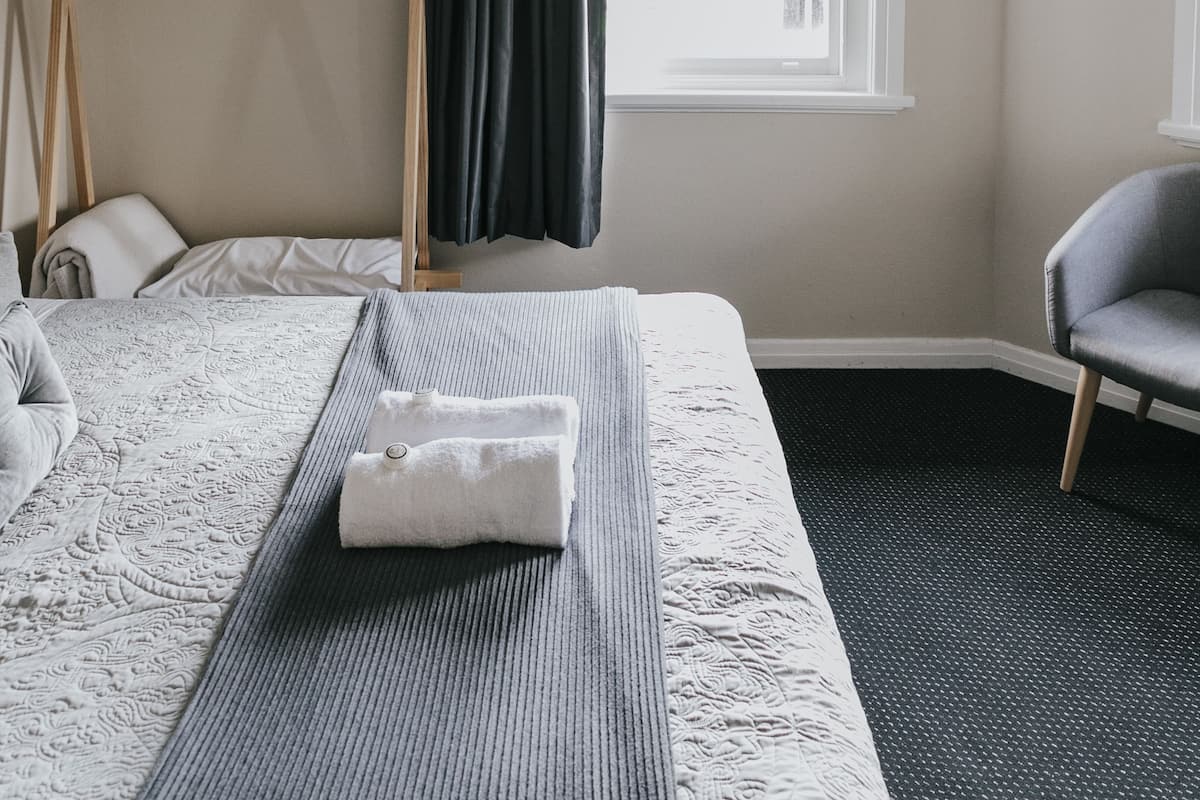 Hotellihuone, jossa on sänky, kattotuuletin, verhoilla varustettu ikkuna, tuoli ja naulakko.