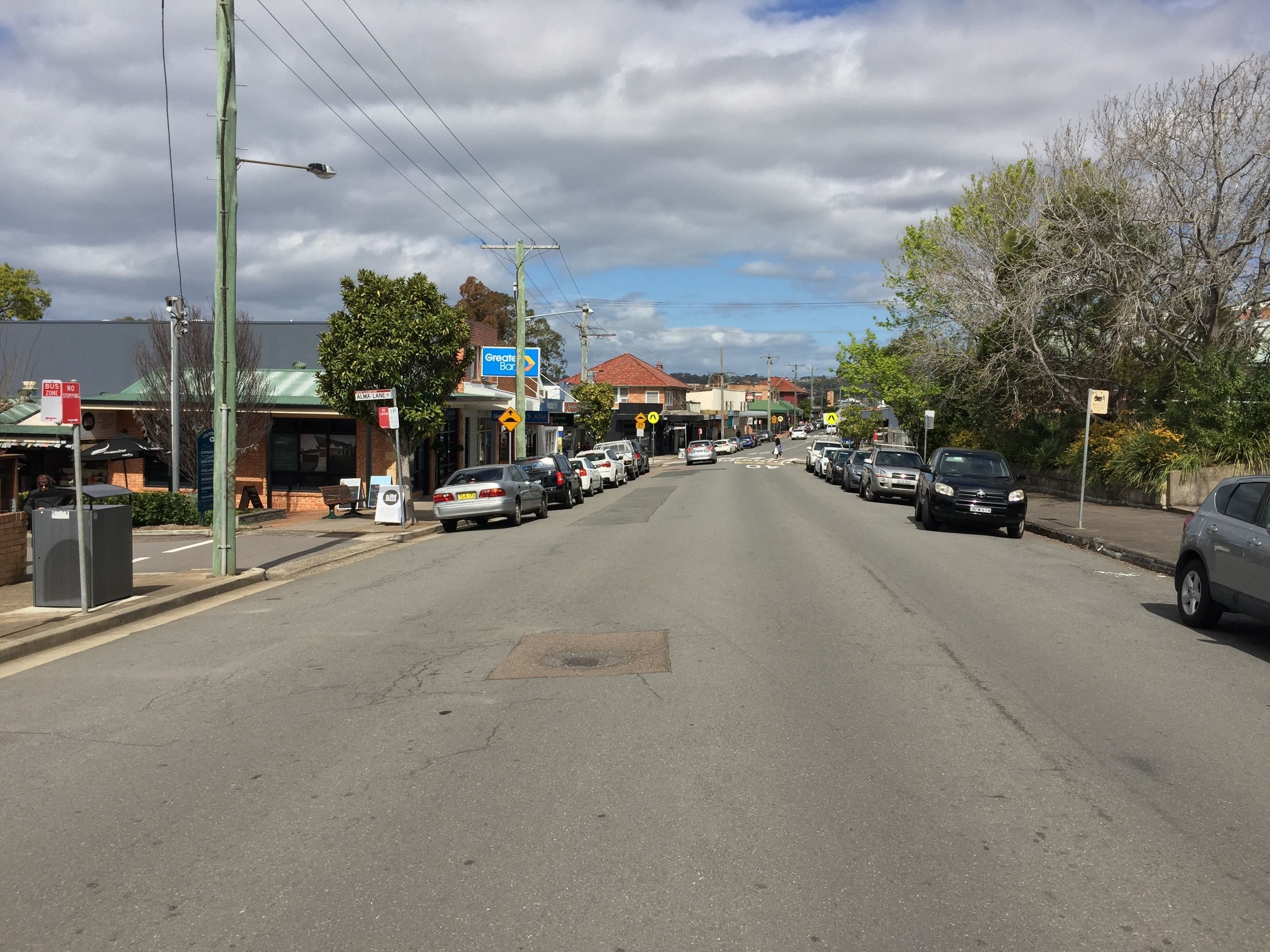 A street view with parked cars, a bus stop, and a building with a sign that reads "Greville."