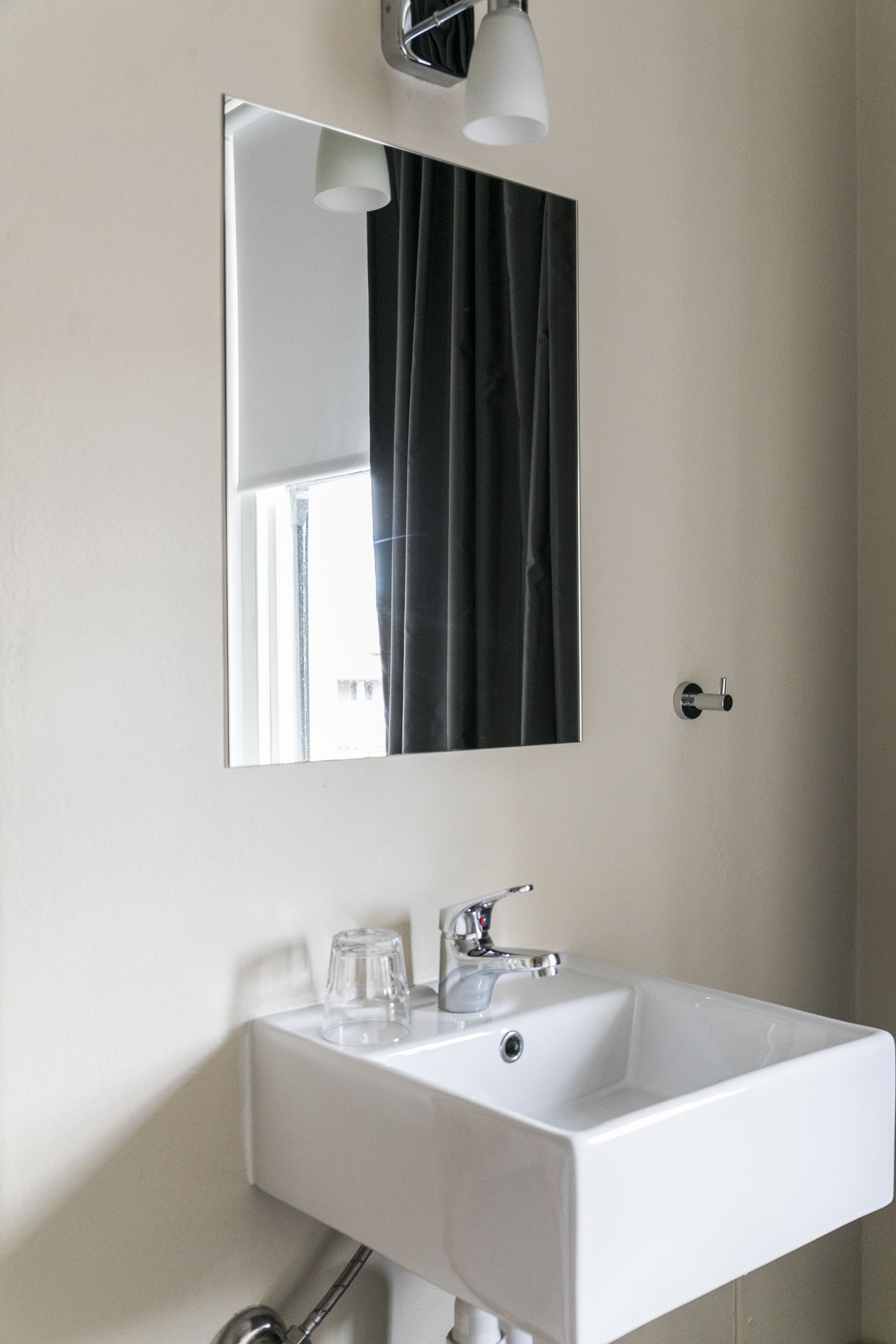 Une salle de bain avec un lavabo blanc, un miroir et un luminaire.