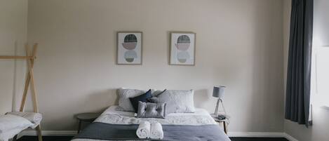 Habitación de hotel impecable con cama, almohadas, una colcha, una mesita de noche con lámpara y dos cuadros enmarcados en la pared.