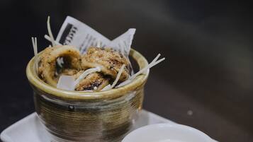 A bowl of fried food with a lime wedge and a small dish of sauce on a white plate.