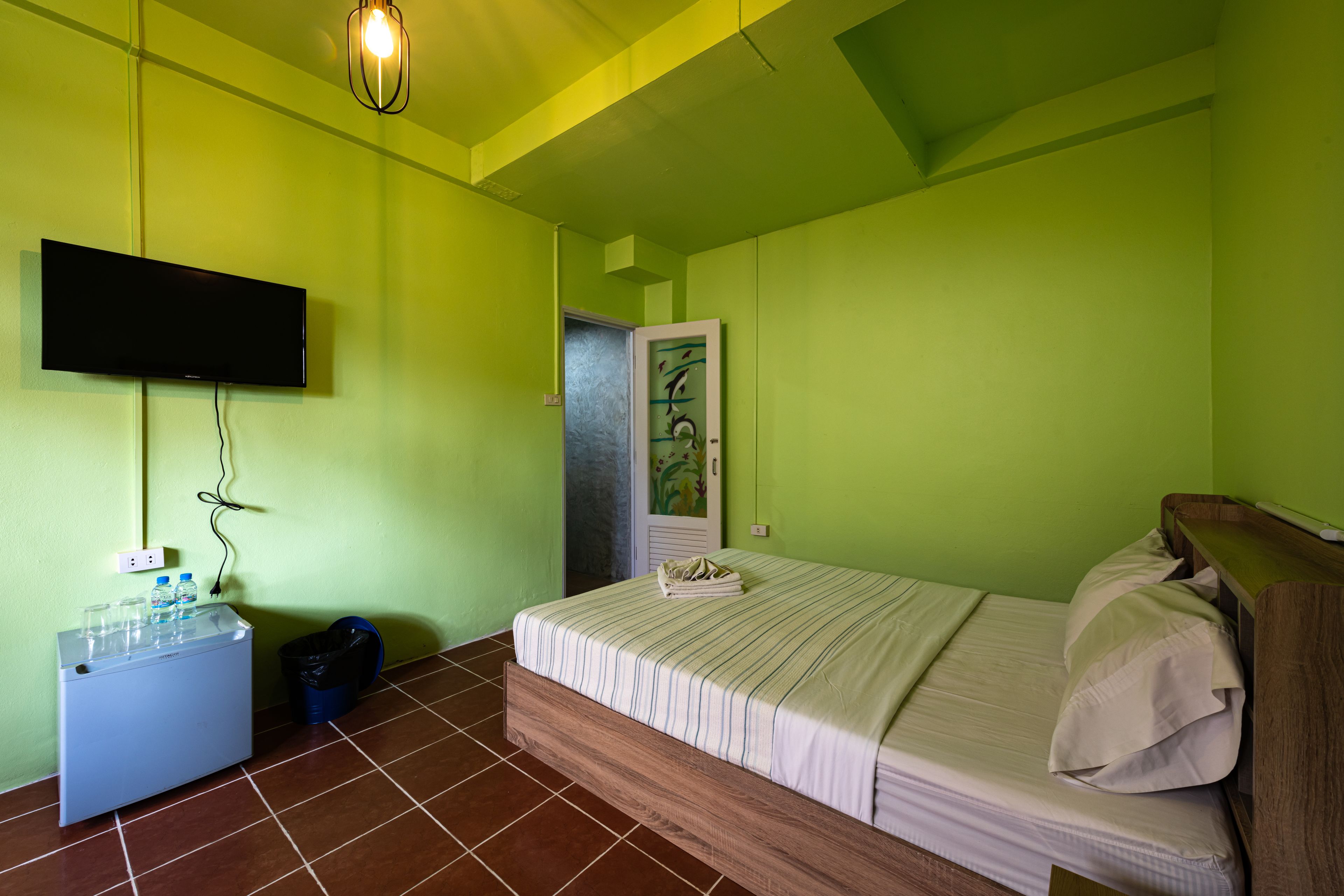 Quarto com cama, televisão fixada na parede, mesinha com tomada e lixeira.
