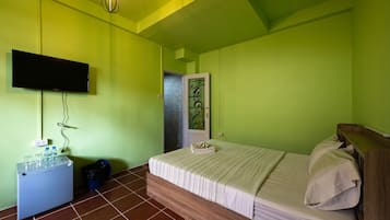Quarto com cama, televisão fixada na parede, mesinha com tomada e lixeira.