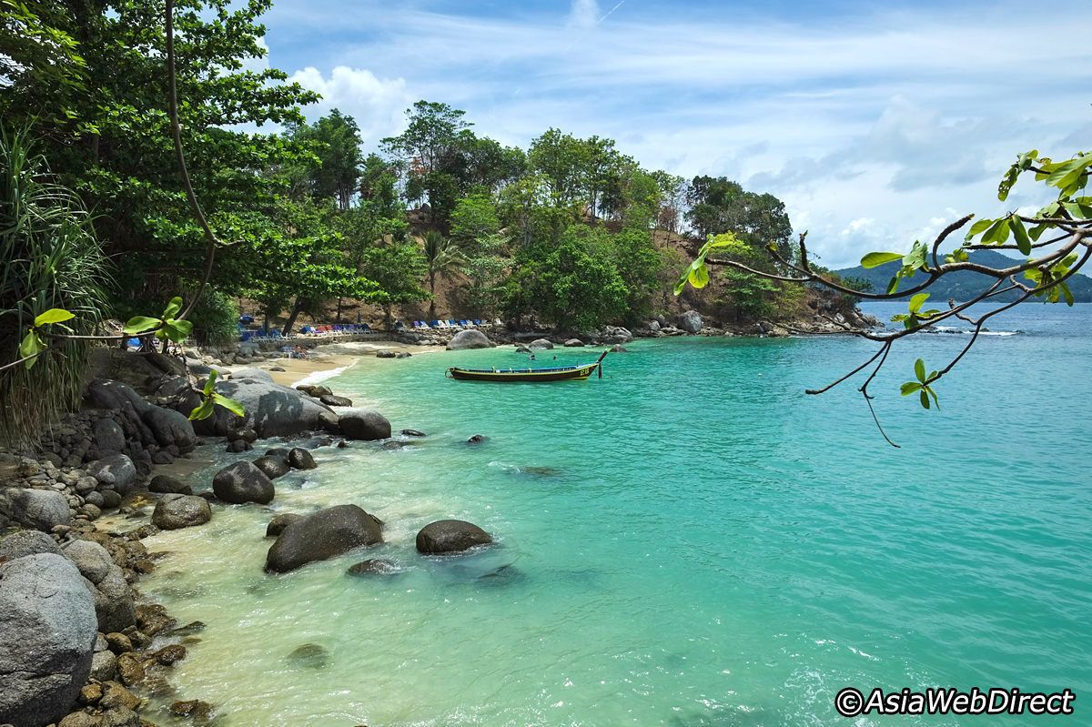 Una playa con agua turquesa cristalina, rocas y un bote.