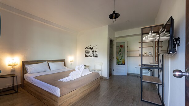 Ein Schlafzimmer mit einem hölzernen Bett, Nachttischlampen, einem an der Wand montierten Fernseher und einem Spiegel mit Kleiderstange.